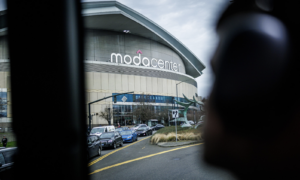 Moda Center exterior with a curved facade and a line of cars driving by on a cloudy day.