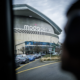 Moda Center exterior with a curved facade and a line of cars driving by on a cloudy day.