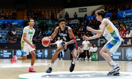 USA basketball player dribbles toward the basket while two defenders close in during a game in an indoor arena