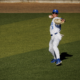 Baseball pitcher in white pinstripe uniform throws a ball on the field, wearing blue cap and sunglasses.
