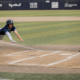 Baseball player in navy uniform slides into home plate as the catcher in blue gear closes in from behind with his glove ready.