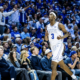 BYU basketball player wearing number 3 in a white uniform runs down the court as a packed crowd in blue cheers in the background.