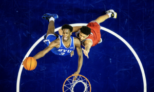 Overhead view of two basketball players contesting for the ball above the hoop, blue BYU jersey vs red jersey.