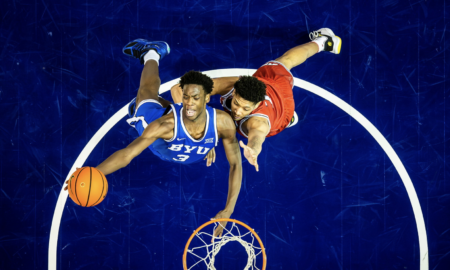 Overhead view of two basketball players contesting for the ball above the hoop, blue BYU jersey vs red jersey.
