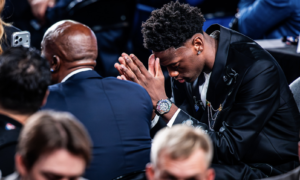 Young man in a black suit bows his head with hands pressed together in prayer at a formal event.