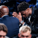 Young man in a black suit bows his head with hands pressed together in prayer at a formal event.