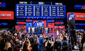NBA Draft 2026 stage with players lined up on a red-carpet, large draft board above the crowd on screens.
