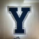 Large navy Y sign with a white glowing edge mounted on a beige paneled wall.