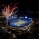 Aerial night view of a crowded football stadium with colorful fireworks above and a blue ‘GO COUGS’ display in the stands.