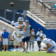 BYU football player in white jumps to catch an airborne ball as a teammate on the ground and spectators watch in the background.