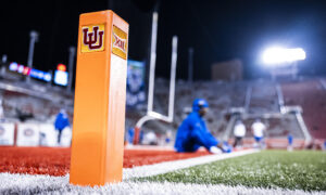 Close-up of an orange football field pylon with the Indiana University logo, blurred players and bright stadium lights in the background.