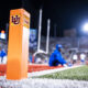 Close-up of an orange football field pylon with the Indiana University logo, blurred players and bright stadium lights in the background.