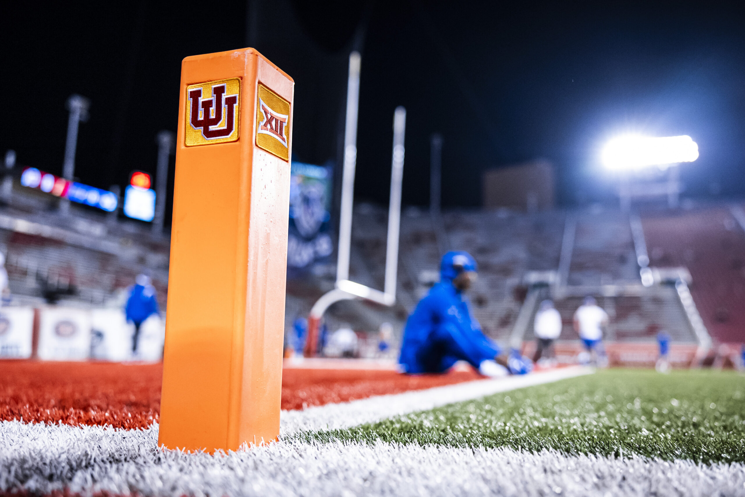 Close-up of an orange football field pylon with the Indiana University logo, blurred players and bright stadium lights in the background.