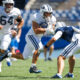 Football players in white uniforms chase a ball carrier during a daytime game; BYU logo visible on the helmet.