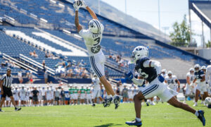 Football player in white jumps to catch the ball during a game, with blue stadium seats in the background.