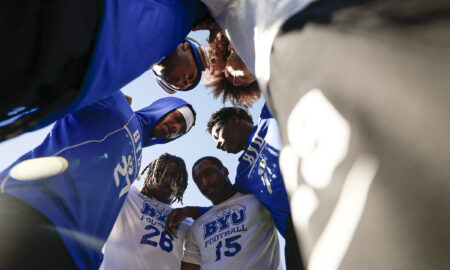 Group of football players in blue and white jerseys forming a low huddle, heads together, viewed from below]