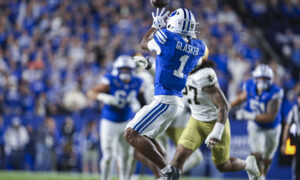 Football player in blue jersey leaps to catch the ball in a crowded stadium, crowd in blue in background.