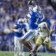 Football player in blue jersey leaps to catch the ball in a crowded stadium, crowd in blue in background.