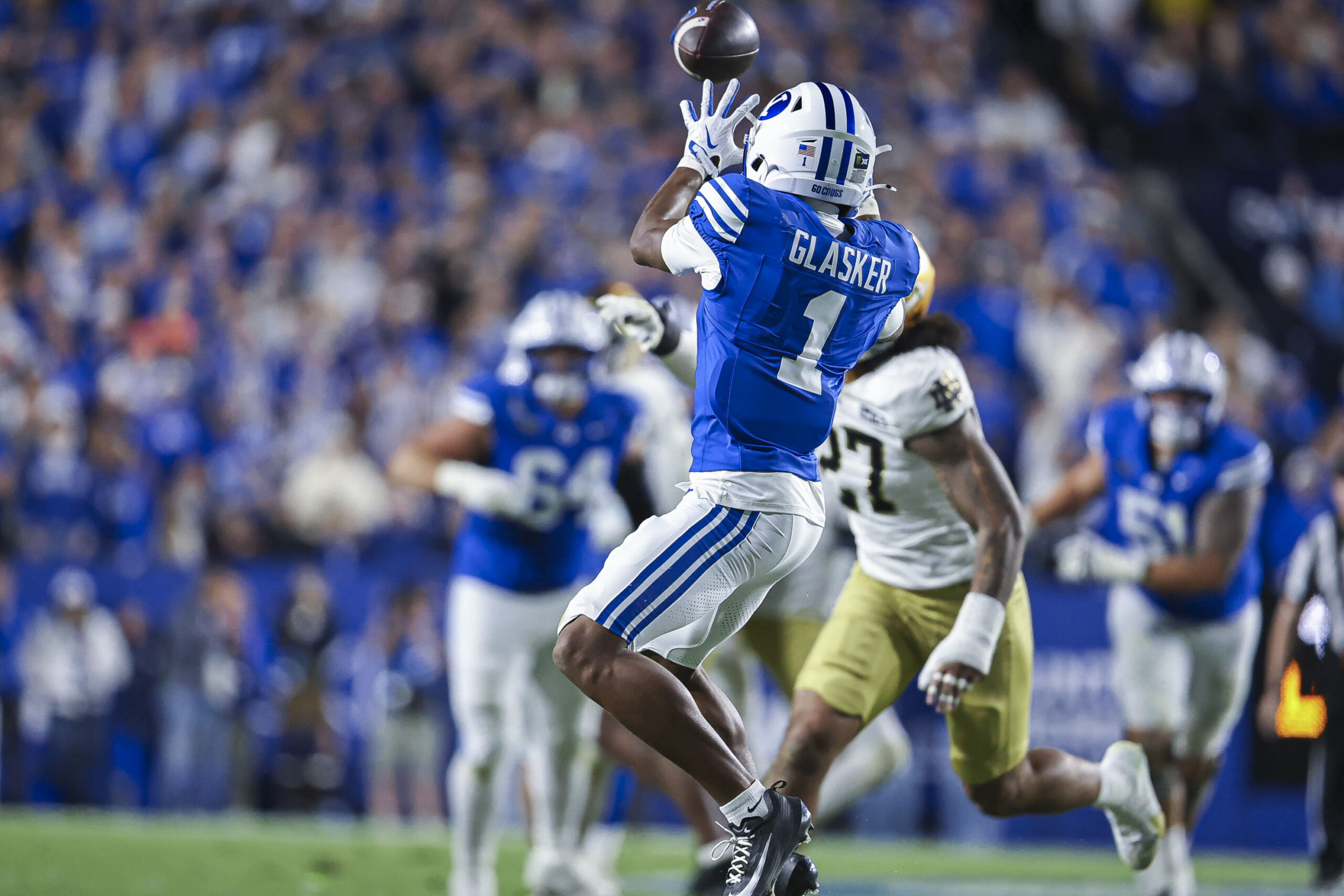 Football player in blue jersey leaps to catch the ball in a crowded stadium, crowd in blue in background.
