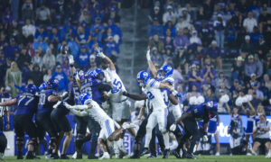Football players in blue and white leap for a loose ball as a crowd looks on from the stands.