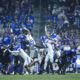 Football players in blue and white leap for a loose ball as a crowd looks on from the stands.