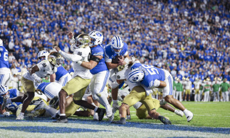 College football players from BYU and Notre Dame clash for the ball as fans fill the blue stadium seating behind them.