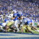 College football players from BYU and Notre Dame clash for the ball as fans fill the blue stadium seating behind them.