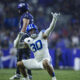 BYU football player in blue and white uniform celebrating with arms raised on the field, crowd blurred in background