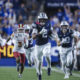 CSU BYU football player in blue jersey carrying ball, sprinting toward field with crowd in blue stands behind him.